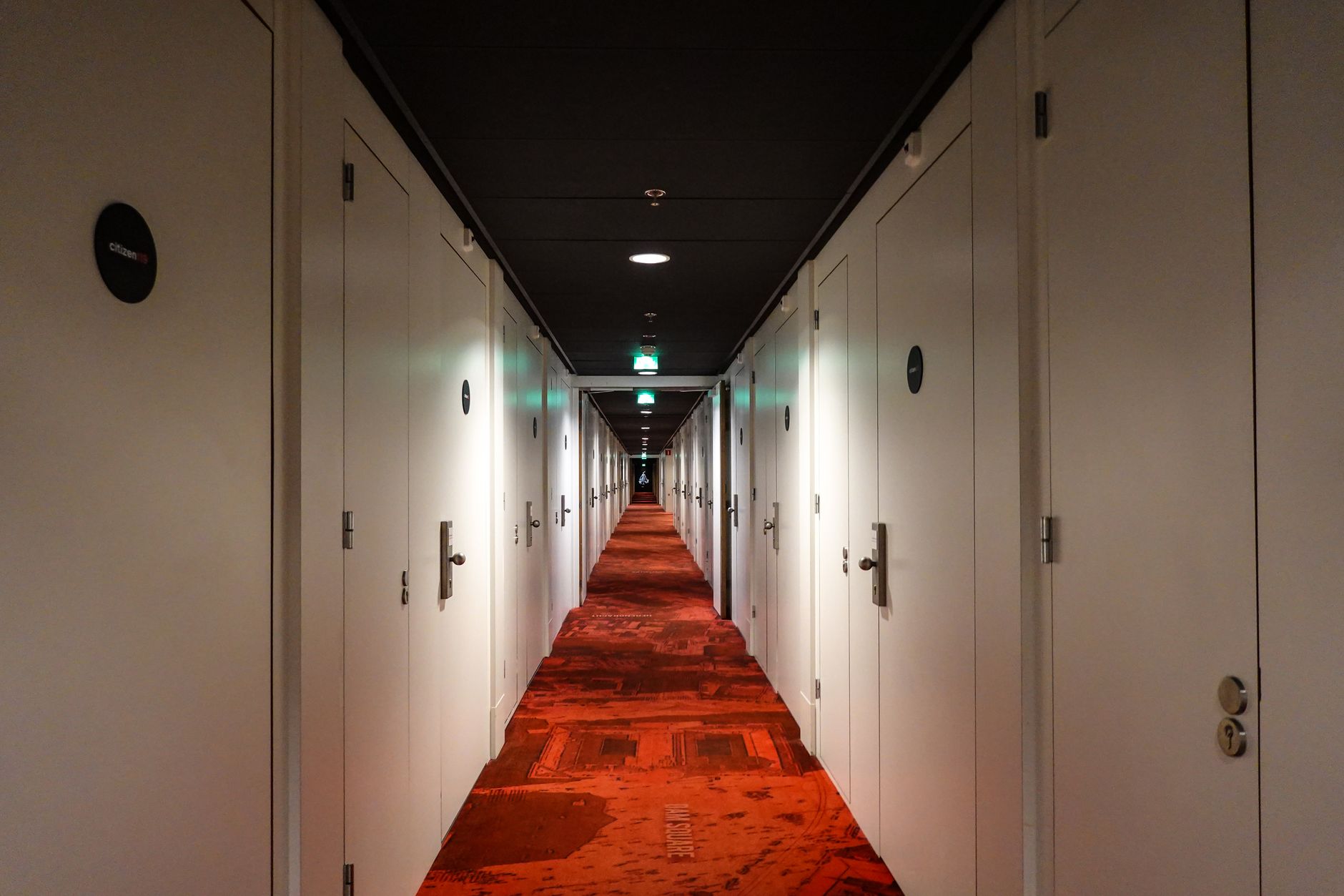 Lang hotelgang med rødt tæppe og døre på begge sider